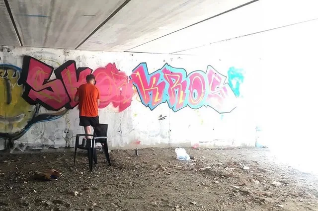 Artist painting pink and blue graffiti lettering on a wall